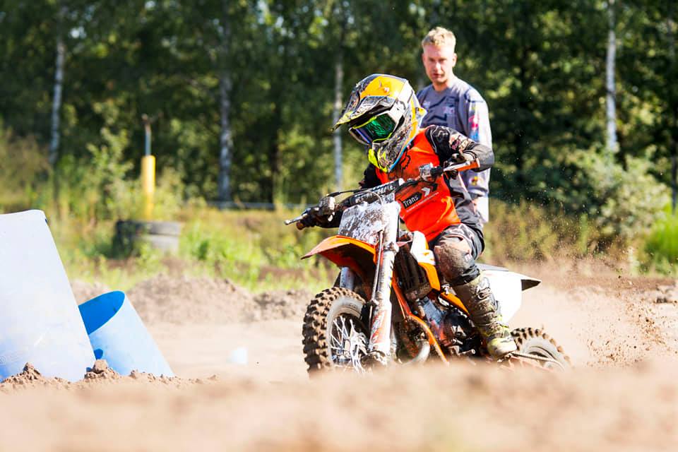 Foto van een kleine motocrosser (kindje) met op de achtergrond trainer Kevon Van Geldorp